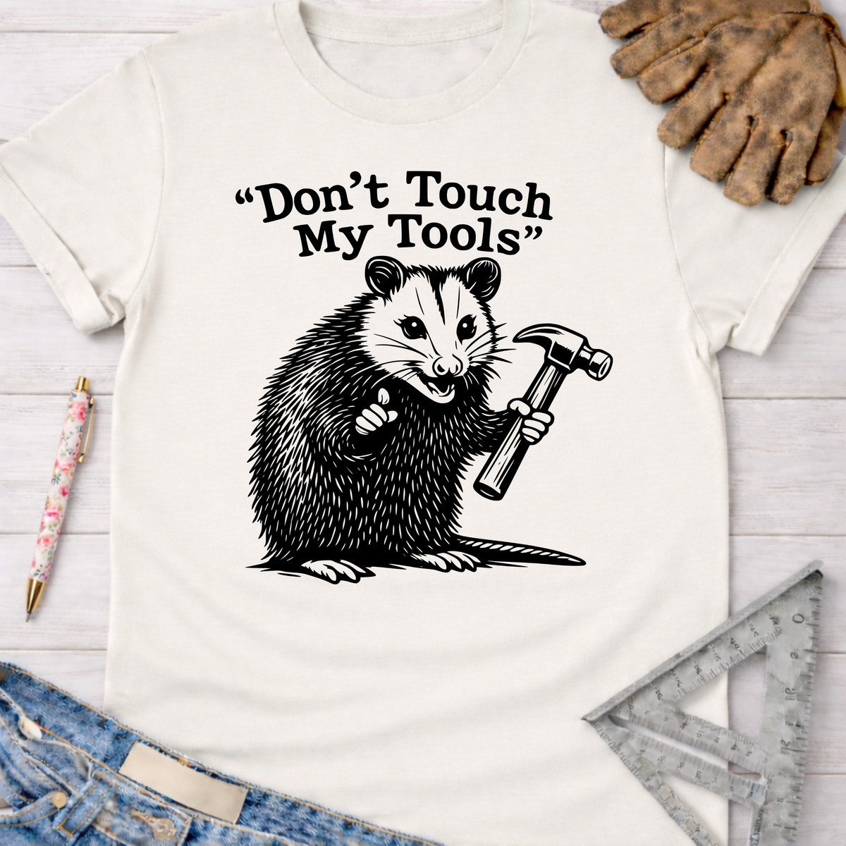 Women's funny woodworking graphic tee shirt for female woodworkers, makers, and DIY builders — Sawdust & Ponytails. Cream t-shirt with a black graphic of an opossum holding a hammer and "Don't Touch My Tools" text.