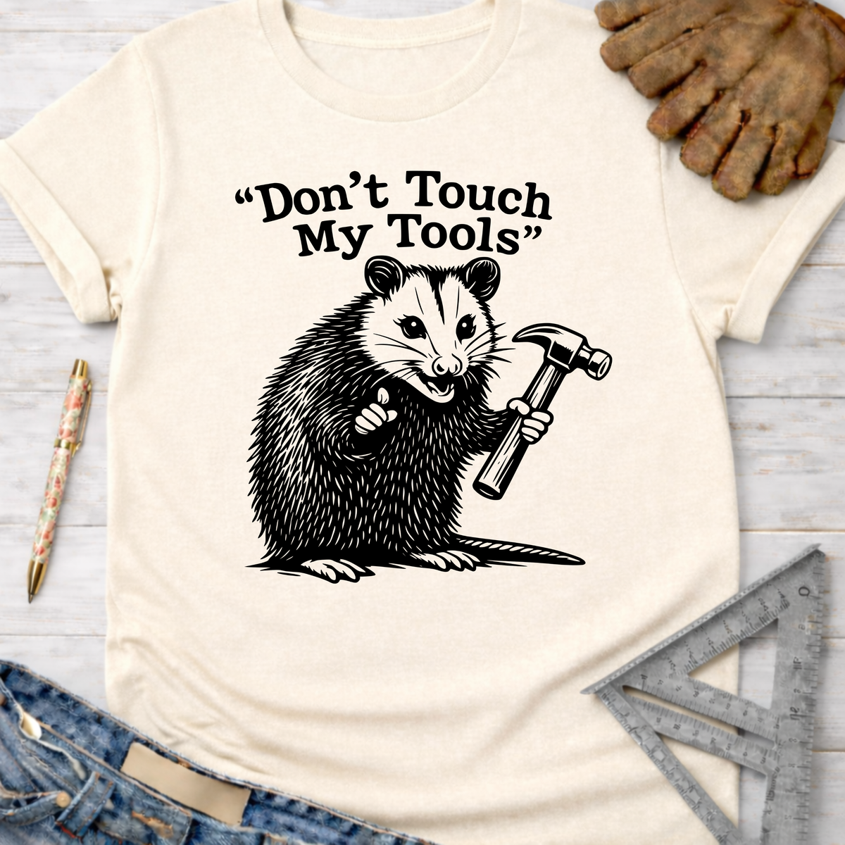 Women's funny woodworking graphic tee shirt for female woodworkers, makers, and DIY builders — Sawdust & Ponytails. Cream t-shirt with a black graphic of an opossum holding a hammer and the text "Don't Touch My Tools".