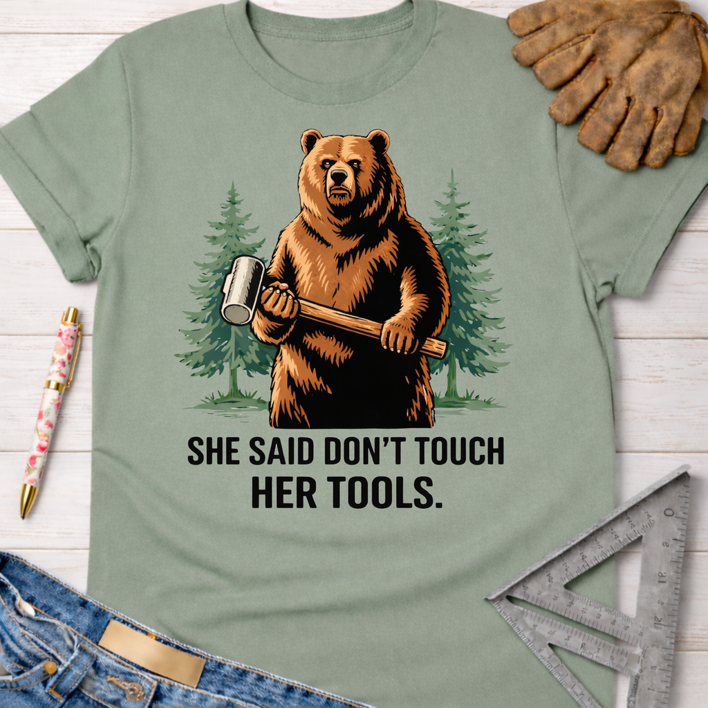 Women's funny woodworking graphic tee shirt for female woodworkers, makers, and DIY builders — Sawdust & Ponytails. Sage green cotton tee with a bear holding a mallet and "SHE SAID DON'T TOUCH HER TOOLS." text.