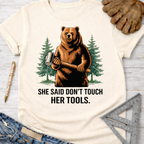 Women's funny woodworking graphic tee shirt for female woodworkers, makers, and DIY builders — Sawdust & Ponytails. Cream t-shirt with a bear holding a mallet and "SHE SAID DON'T TOUCH HER TOOLS." text.
