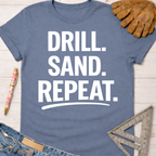 Women's funny woodworking graphic tee shirt for female woodworkers, makers, and DIY builders — Sawdust & Ponytails. Blue cotton tee with "DRILL. SAND. REPEAT." in white text.