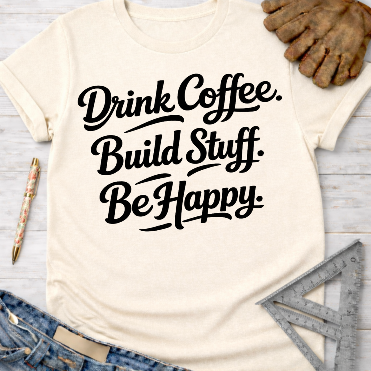 Women's funny woodworking graphic tee shirt for female woodworkers, makers, and DIY builders — Sawdust & Ponytails. Cream t-shirt with "Drink Coffee. Build Stuff. Be Happy." in black script.