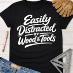 Women's funny woodworking graphic tee shirt for female woodworkers, makers, and DIY builders — Sawdust & Ponytails. Black cotton tee with "Easily Distracted by Wood & Tools" in white script.