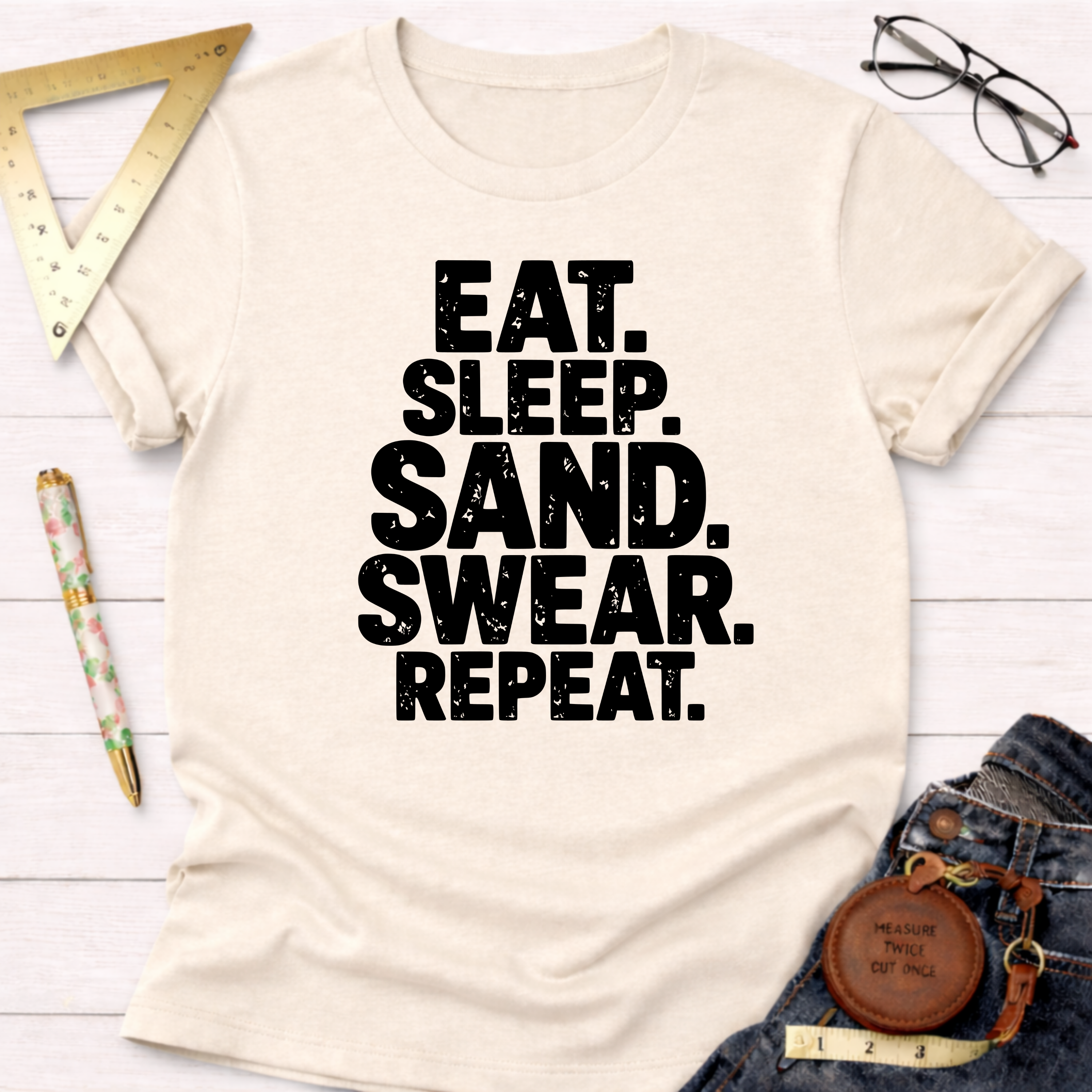 Cream cotton t-shirt with "Eat. Sleep. Sand. Swear. Repeat." in bold black text.