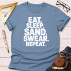 Blue cotton t-shirt with "EAT. SLEEP. SAND. SWEAR. REPEAT." in white text, styled with jeans.