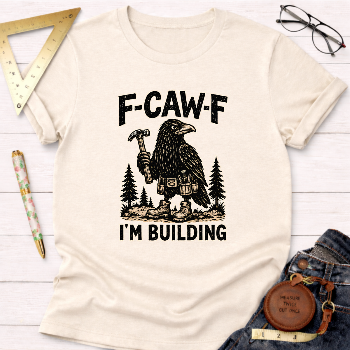 Cream "F-CAW-F, I'm Building" t-shirt with a crow holding a hammer and wearing a tool belt.
