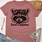 Mauve Feral Carpenter T-shirt with a raccoon wearing sunglasses graphic. Women's funny woodworking graphic tee shirt for female woodworkers, makers, and DIY builders — Sawdust & Ponytails.