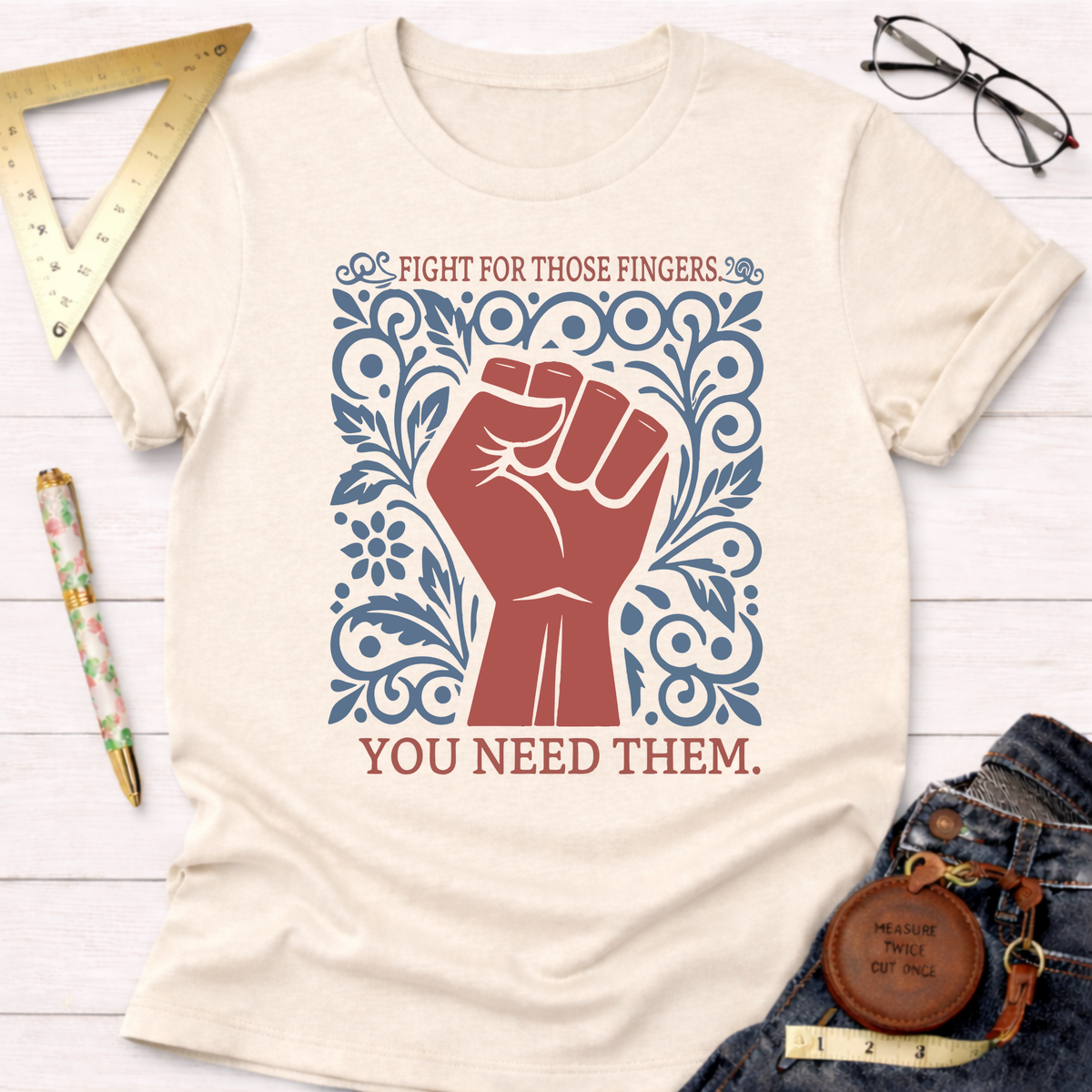 Cream t-shirt with a red fist and blue floral design, text "Fight For Those Fingers You Need Them.