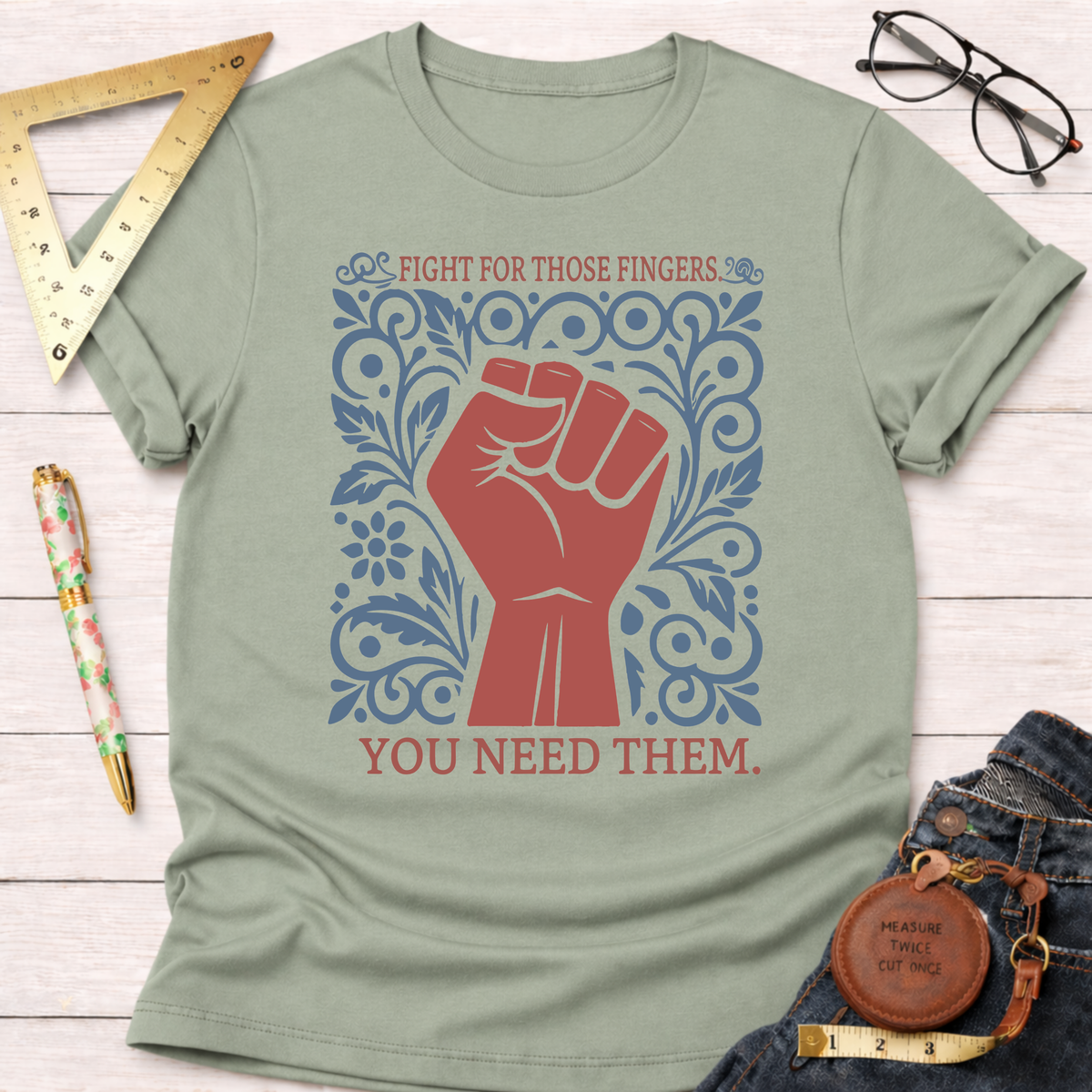Sage green cotton t-shirt with a red fist and blue floral design, "FIGHT FOR THOSE FINGERS. YOU NEED THEM." text.