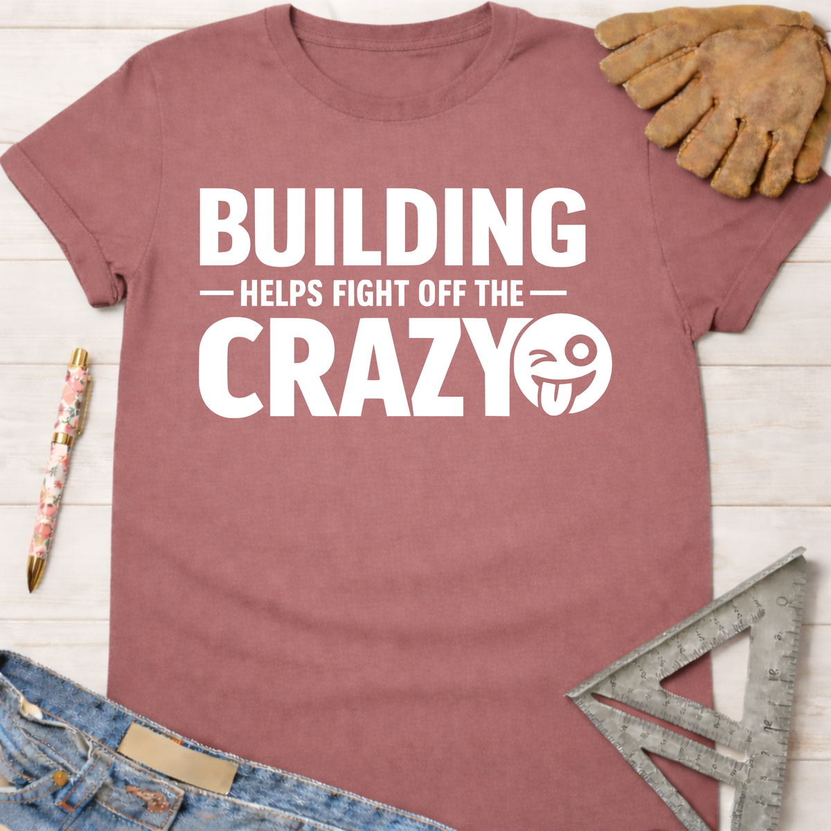 Women's funny woodworking graphic tee shirt for female woodworkers, makers, and DIY builders — Sawdust & Ponytails. Mauve cotton tee with "BUILDING HELPS FIGHT OFF THE CRAZY" text and winking emoji.