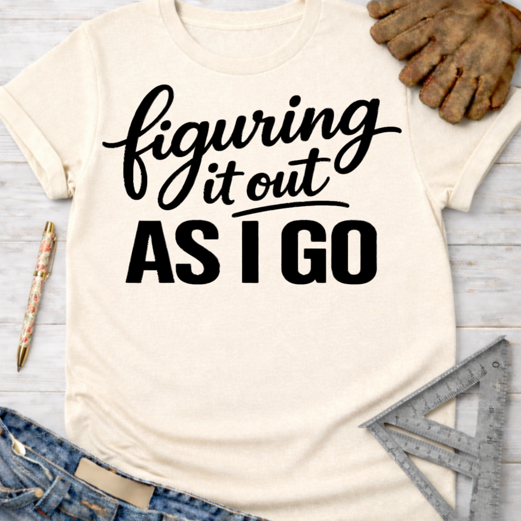 Women's funny woodworking graphic tee shirt for female woodworkers, makers, and DIY builders — Sawdust & Ponytails. Cream t-shirt with "figuring it out AS I GO" in black script.