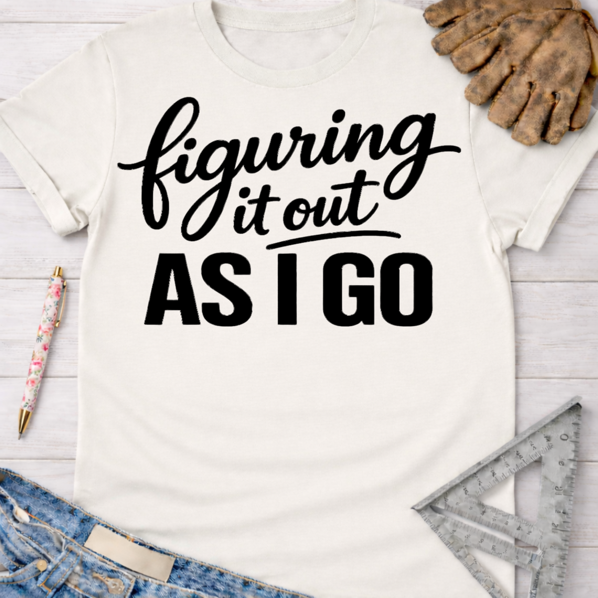 Women's funny woodworking graphic tee shirt for female woodworkers, makers, and DIY builders — Sawdust & Ponytails. Cream t-shirt with "figuring it out AS I GO" in black script and block text.