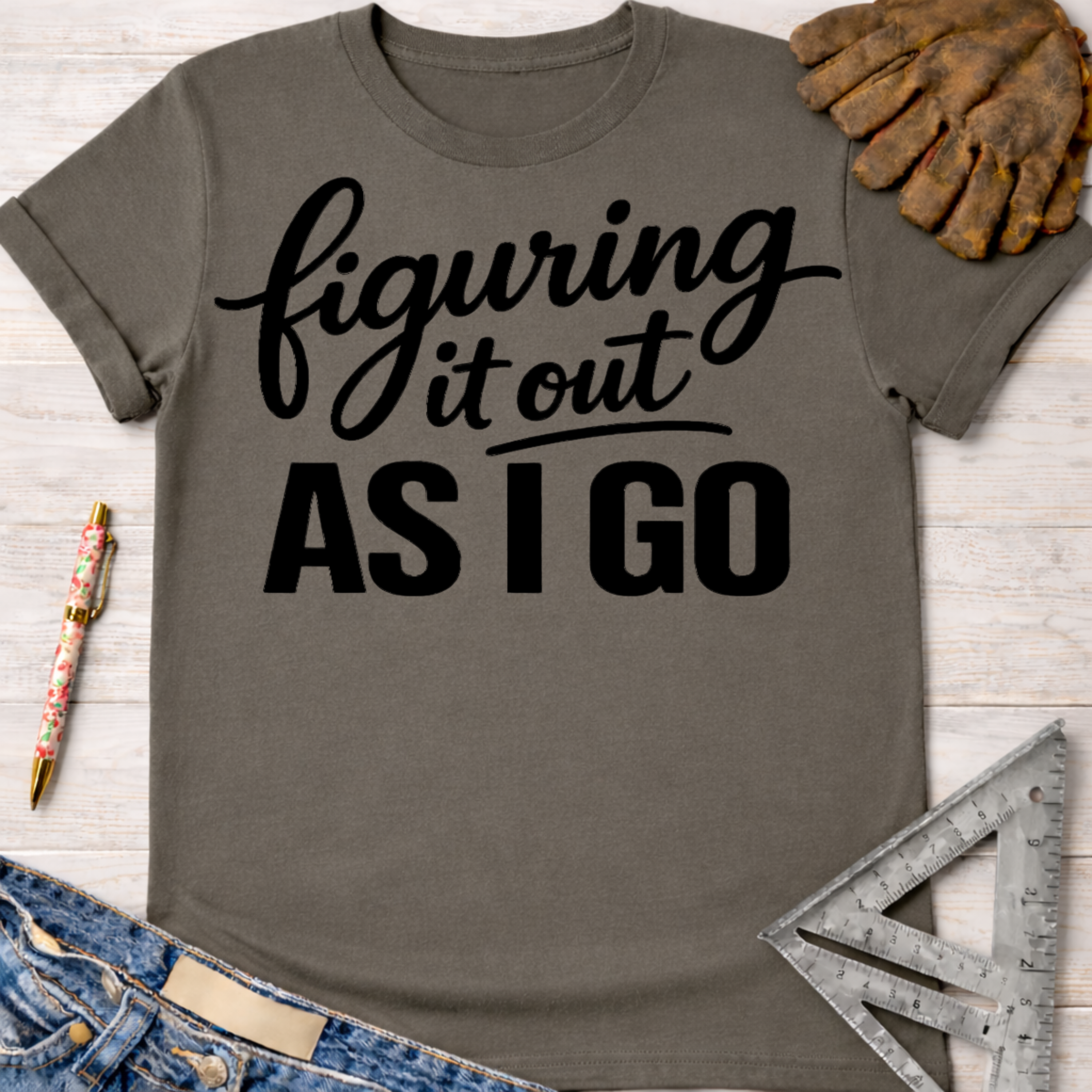 Women's funny woodworking graphic tee shirt for female woodworkers, makers, and DIY builders — Sawdust & Ponytails. Gray cotton t-shirt with "figuring it out AS I GO" in black script.