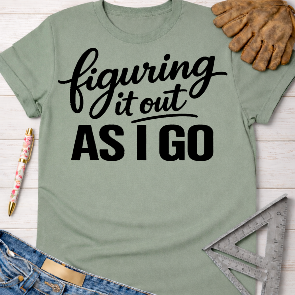 Women's funny woodworking graphic tee shirt for female woodworkers, makers, and DIY builders — Sawdust & Ponytails. Sage green cotton tee with "figuring it out AS I GO" in black script.