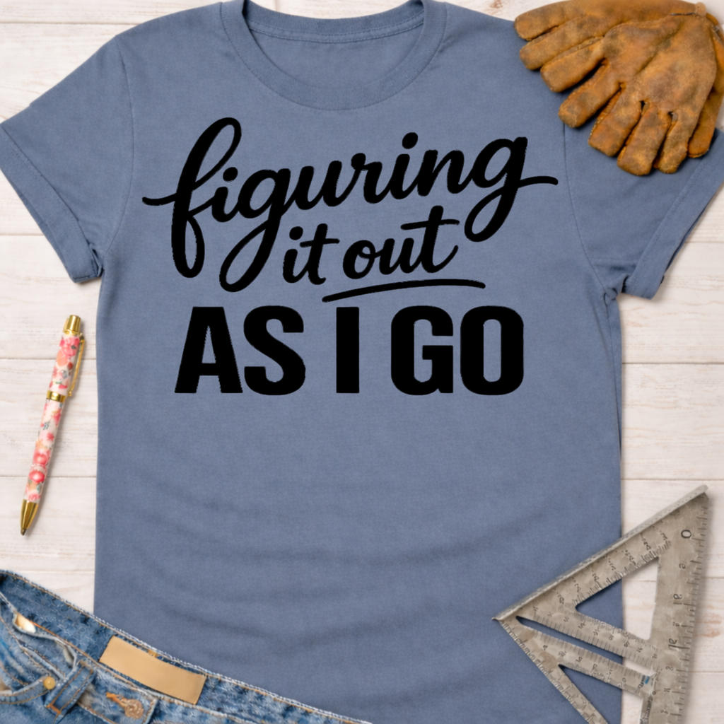 Women's funny woodworking graphic tee shirt for female woodworkers, makers, and DIY builders — Sawdust & Ponytails. Blue cotton tee with "figuring it out AS I GO" in black script.
