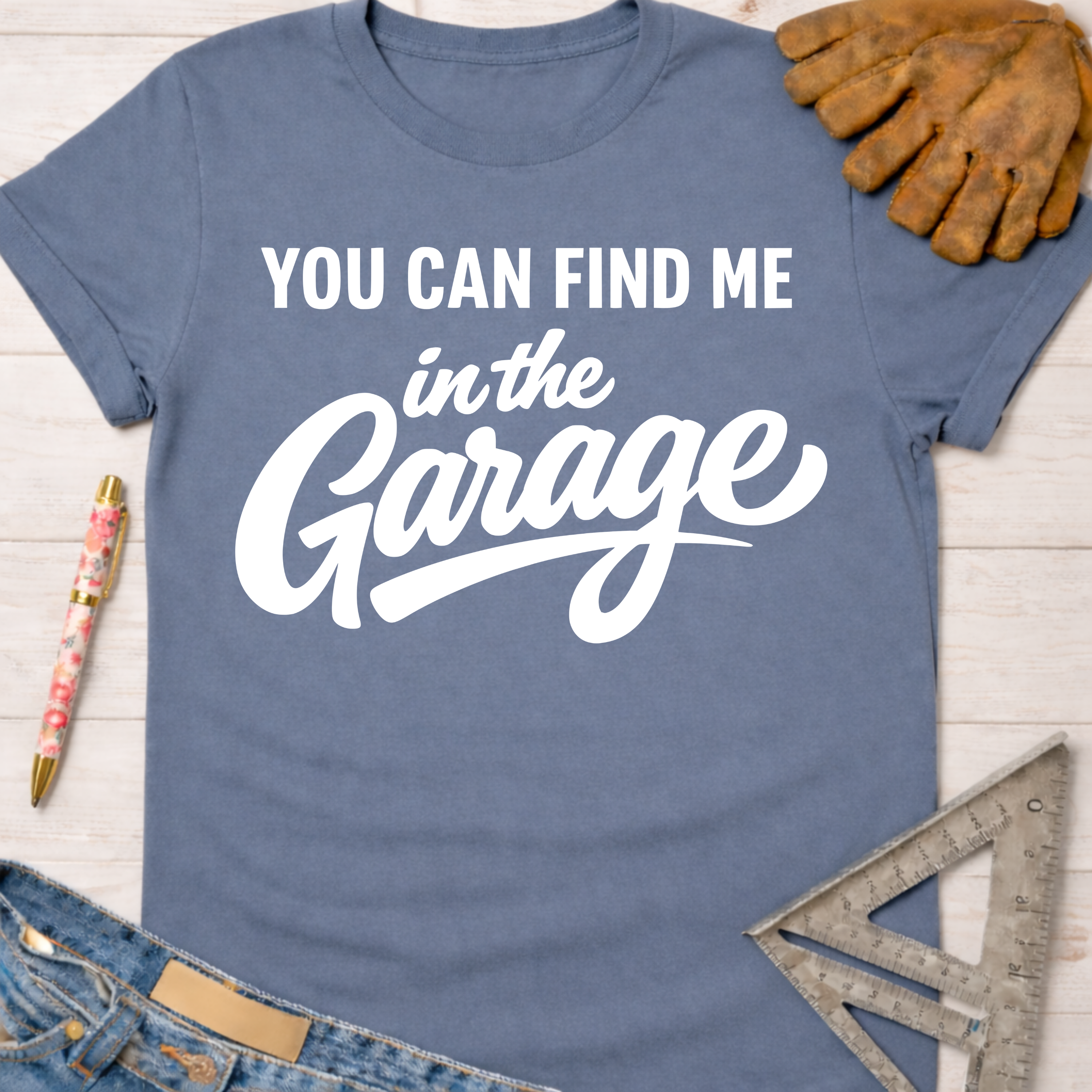 Women's funny woodworking graphic tee shirt for female woodworkers, makers, and DIY builders — Sawdust & Ponytails. Blue crewneck t-shirt with "YOU CAN FIND ME in the Garage" in white text, styled with jeans, gloves, and a ruler.