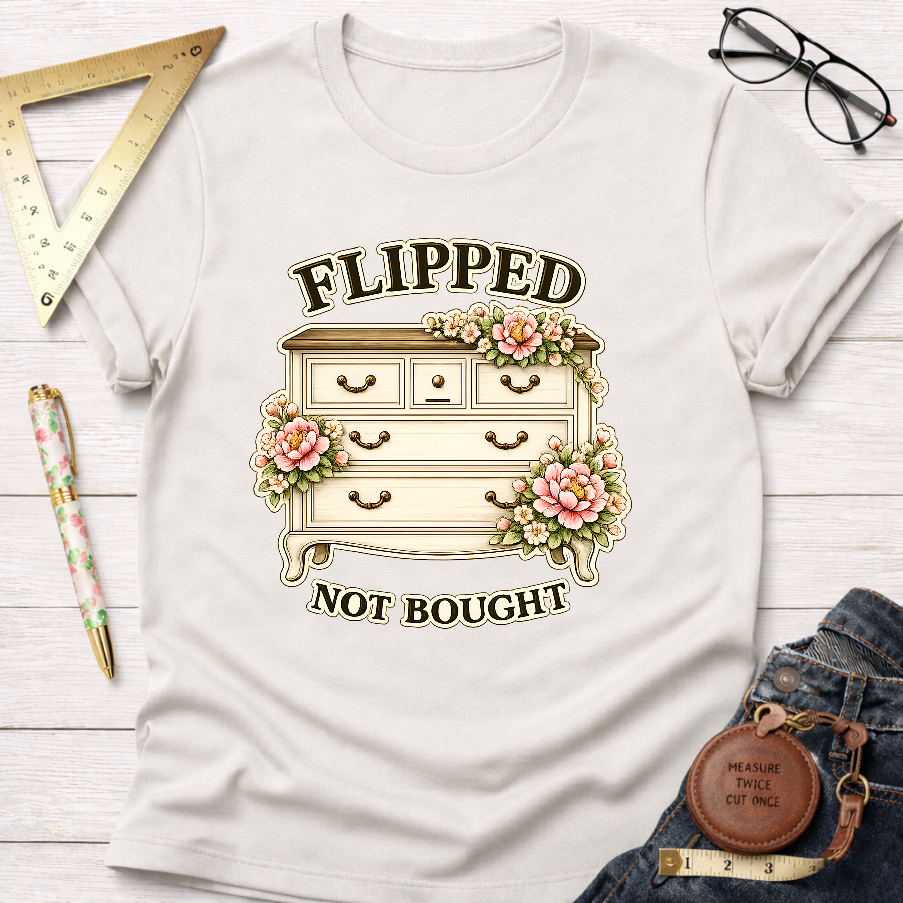 White crew neck t-shirt with "Flipped Not Bought" text and a floral dresser graphic.