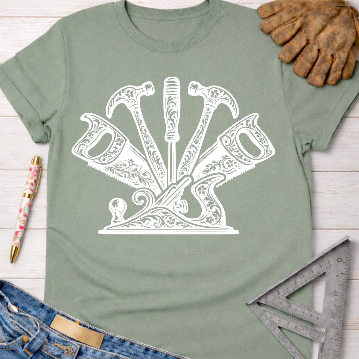 Women's funny woodworking graphic tee shirt for female woodworkers, makers, and DIY builders — Sawdust & Ponytails. Sage green cotton tee with white floral-patterned hammers, saws, screwdriver, and wood plane design.