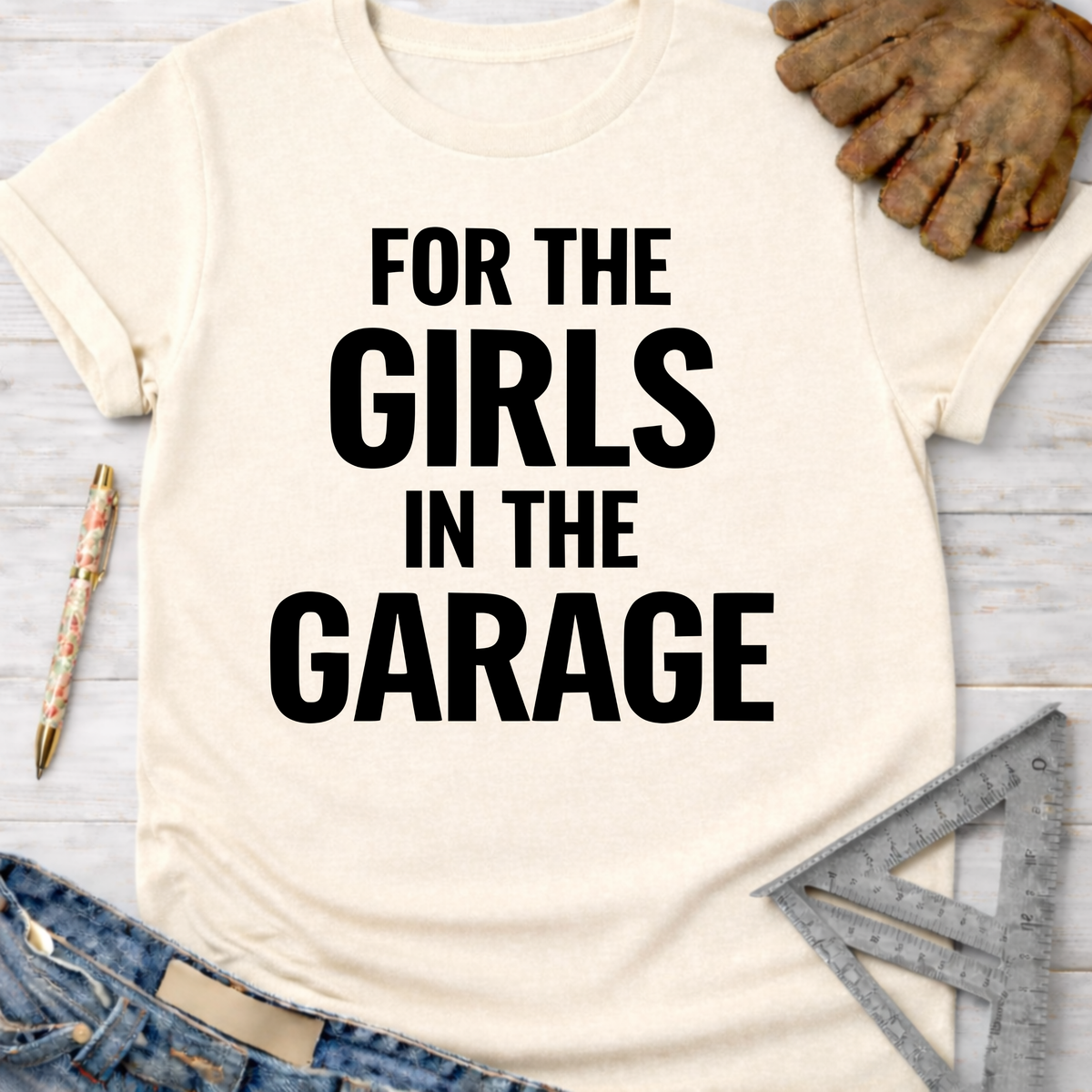 Women's funny woodworking graphic tee shirt for female woodworkers, makers, and DIY builders — Sawdust & Ponytails. Cream t-shirt with "FOR THE GIRLS IN THE GARAGE" in black text.