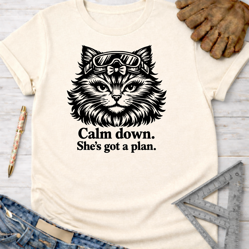 Women's funny woodworking graphic tee shirt for female woodworkers, makers, and DIY builders — Sawdust & Ponytails. Cream tee with a black cat wearing goggles and "Calm down. She's got a plan." text.