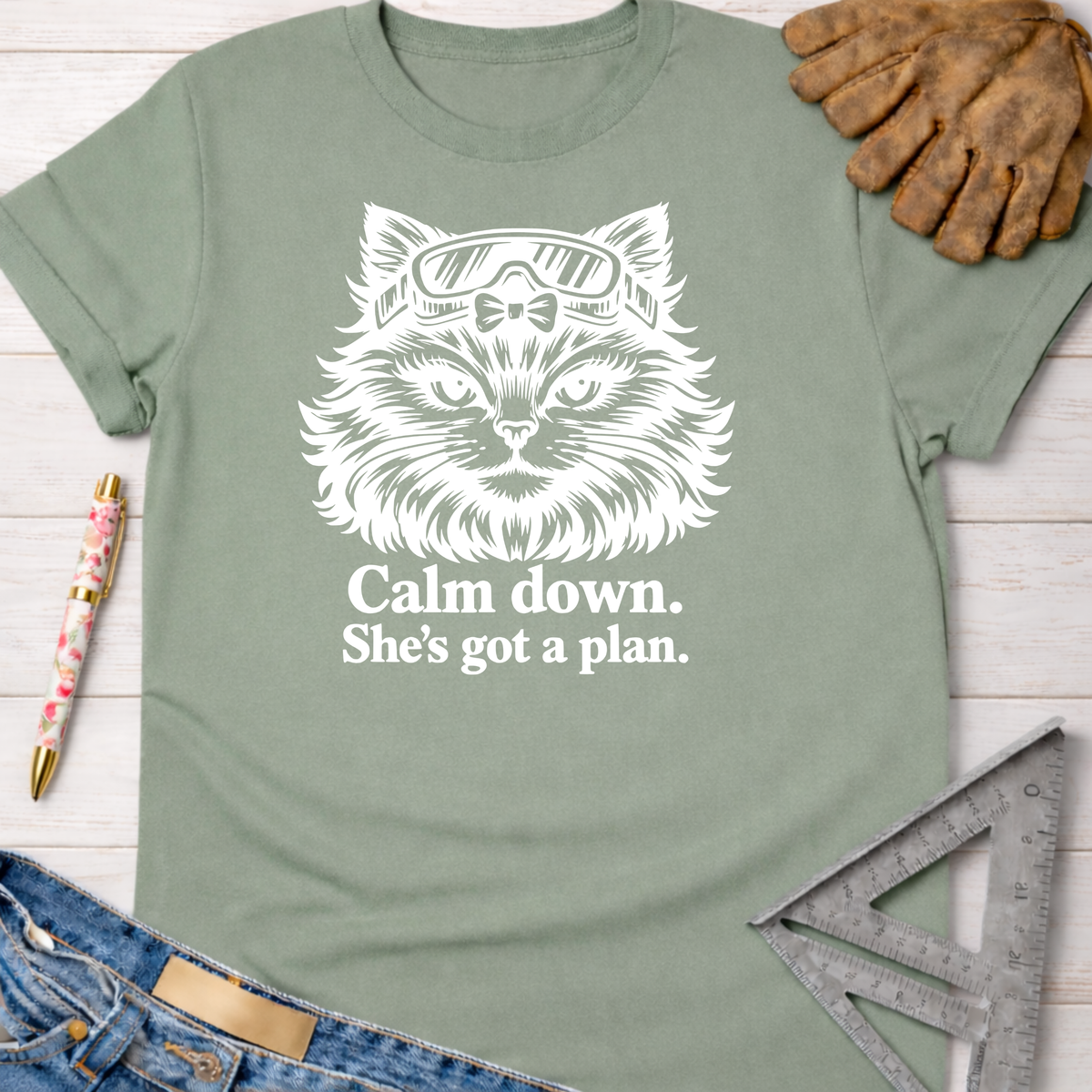 Sage green women's cotton tee with a white graphic of a cat in goggles and text "Calm down. She's got a plan." Women's funny woodworking graphic tee shirt for female woodworkers, makers, and DIY builders — Sawdust & Ponytails