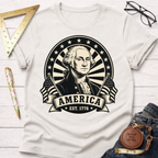 Cream t-shirt with a black and white George Washington portrait, "AMERICA EST. 1776" banner, and flags.