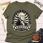 Olive green t-shirt with a black and white George Washington portrait, "AMERICA EST. 1776" banner, and flags.