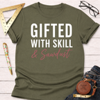 Olive green "Gifted With Skill & Sawdust" t-shirt with white and pink text, folded on a white wood surface.