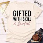 Cream t-shirt with "GIFTED WITH SKILL & Sawdust" text in black and pink, styled with jeans.