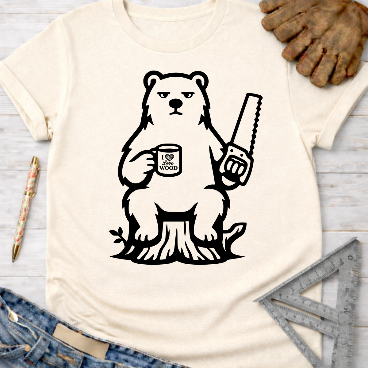Women's funny woodworking graphic tee shirt for female woodworkers, makers, and DIY builders — Sawdust & Ponytails. Cream short-sleeve tee with a black graphic of a grumpy bear holding a saw and "I Love Wood" mug, sitting on a tree stump.