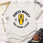 White "Guess What? You Found A Stud" t-shirt with a yellow stud finder graphic, surrounded by carpentry tools.