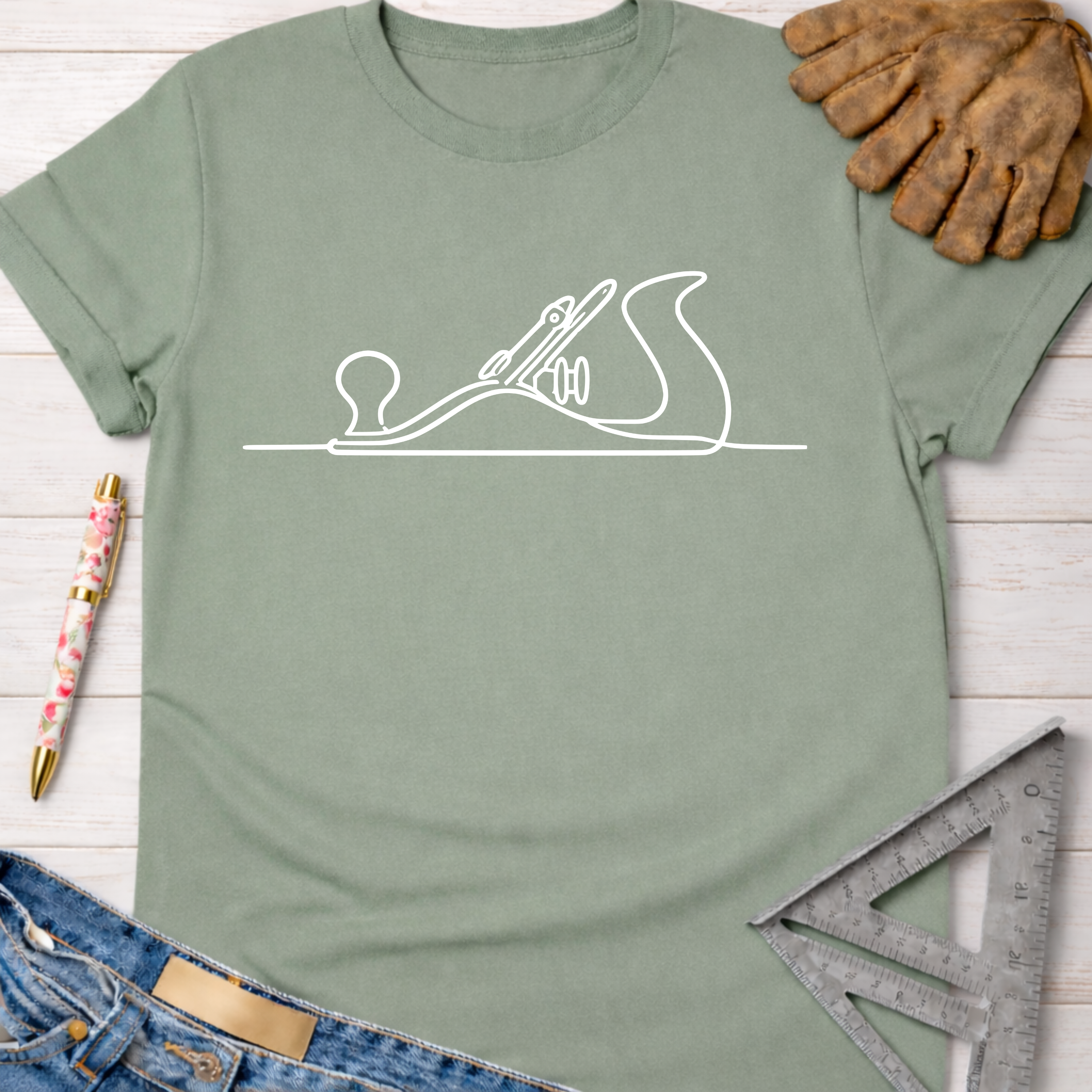 Women's funny woodworking graphic tee shirt for female woodworkers, makers, and DIY builders — Sawdust & Ponytails. Sage green t-shirt with white hand planer line art.