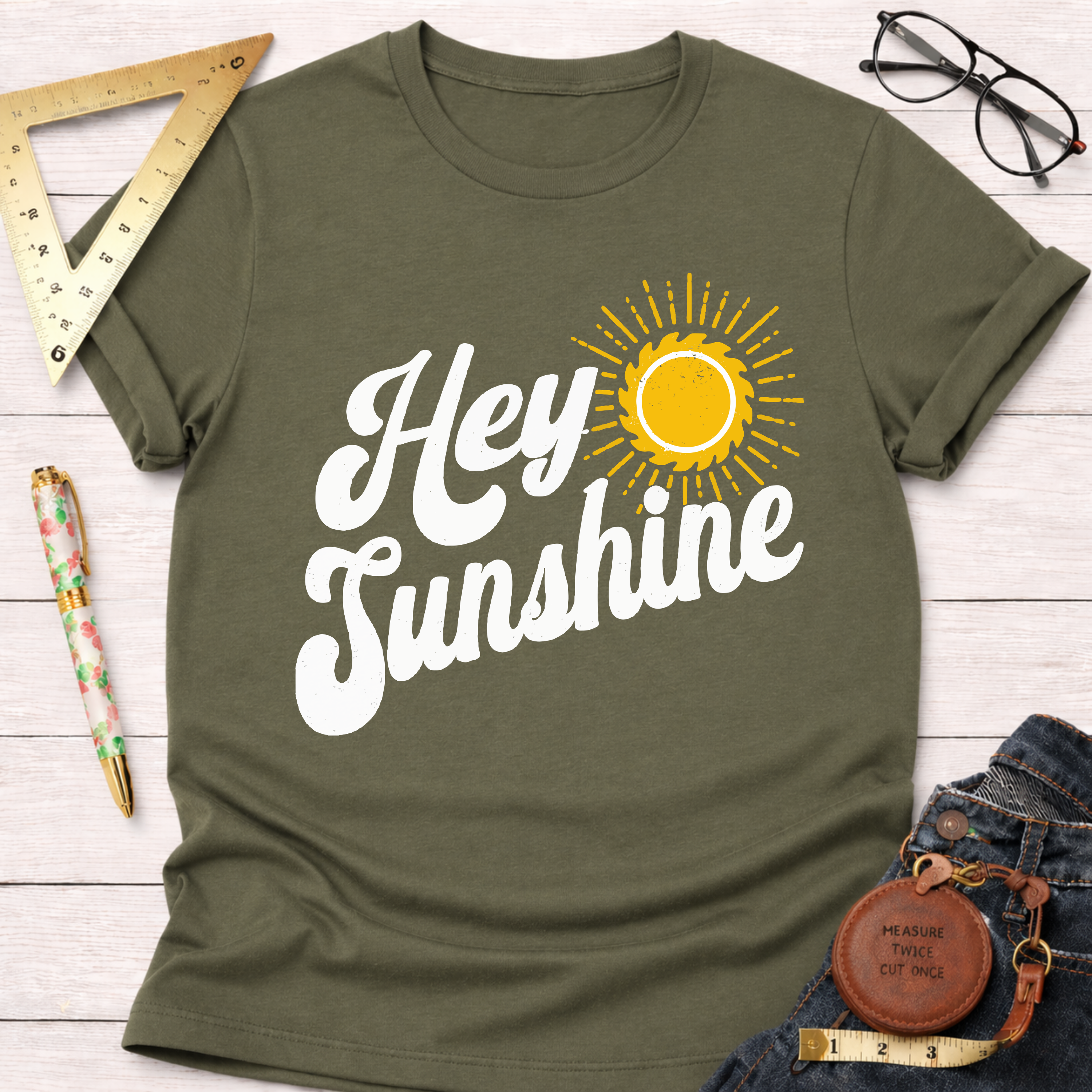 Women's funny woodworking graphic tee shirt for female woodworkers, makers, and DIY builders — Sawdust & Ponytails. Olive green cotton t-shirt with "Hey Sunshine" text and a yellow sun graphic.
