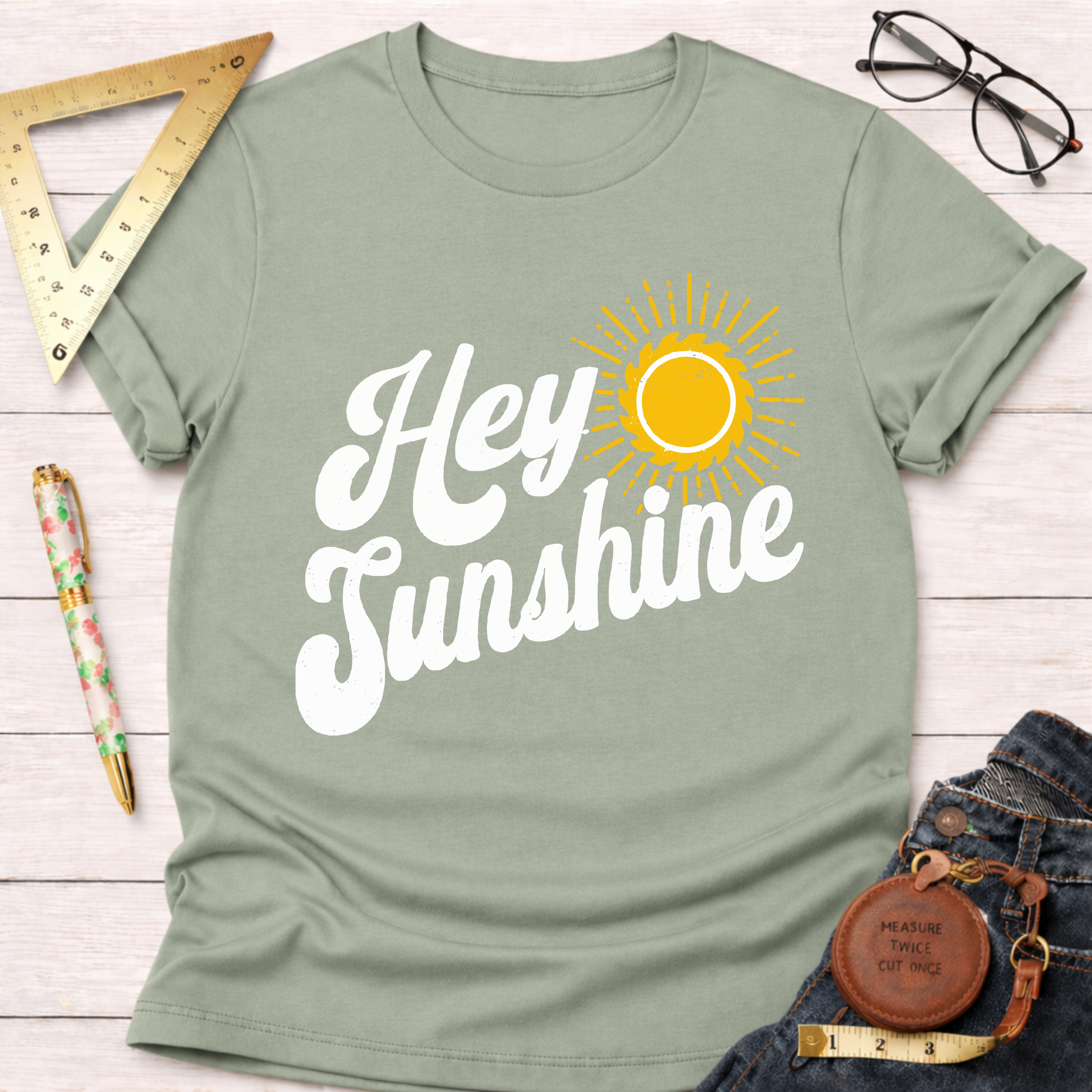 Women's funny woodworking graphic tee shirt for female woodworkers, makers, and DIY builders — Sawdust & Ponytails. Sage green short-sleeve t-shirt with "Hey Sunshine" text and a yellow sun graphic.