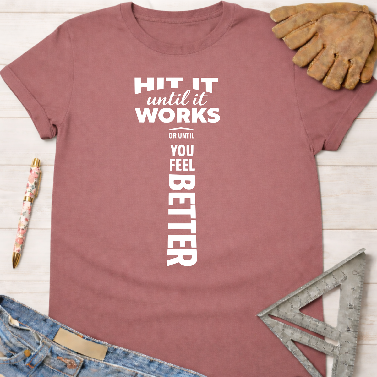 Women's funny woodworking graphic tee shirt for female woodworkers, makers, and DIY builders — Sawdust & Ponytails. Mauve cotton t-shirt with "HIT IT until it works OR UNTIL YOU FEEL BETTER" in white text.