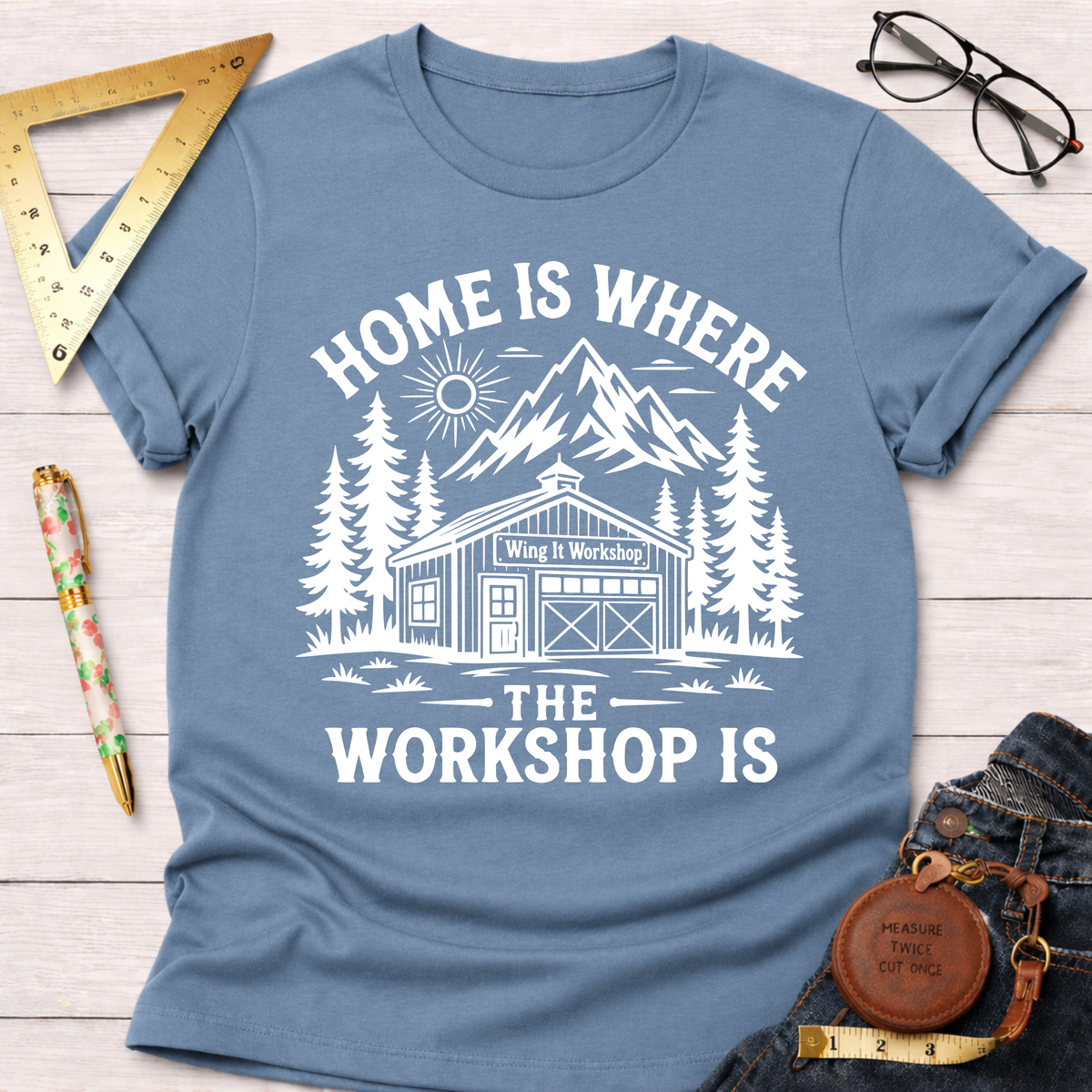 Women's funny woodworking graphic tee shirt for female woodworkers, makers, and DIY builders — Sawdust & Ponytails. Blue cotton tee with "Home Is Where The Workshop Is" graphic.