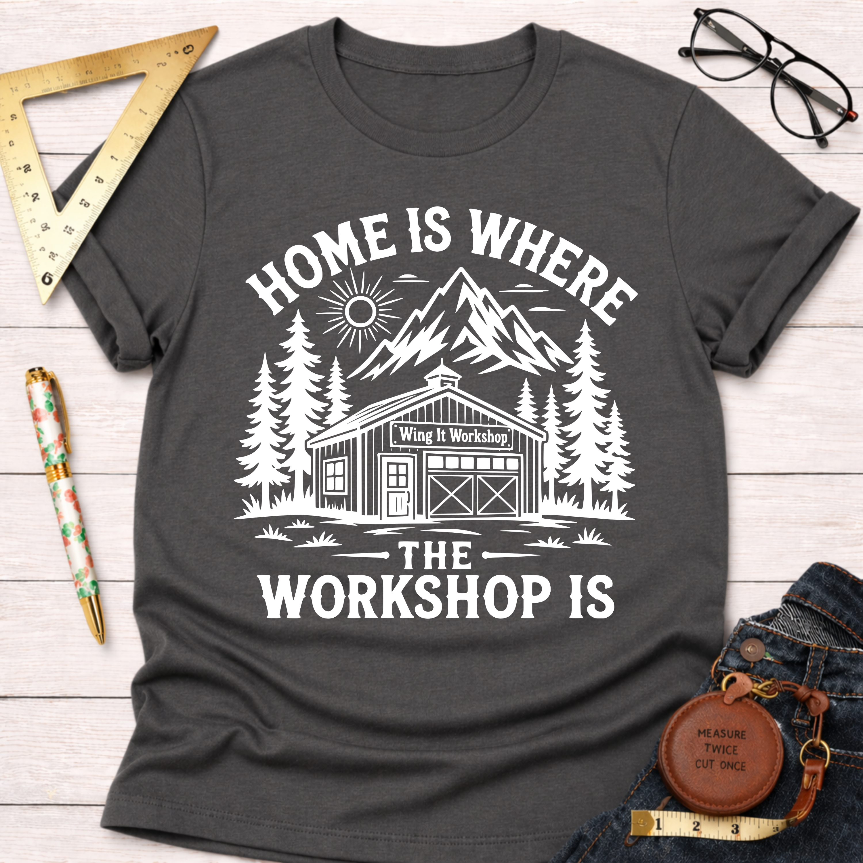 Women's funny woodworking graphic tee shirt for female woodworkers, makers, and DIY builders — Sawdust & Ponytails. Dark gray cotton tee with "Home Is Where The Workshop Is" graphic.