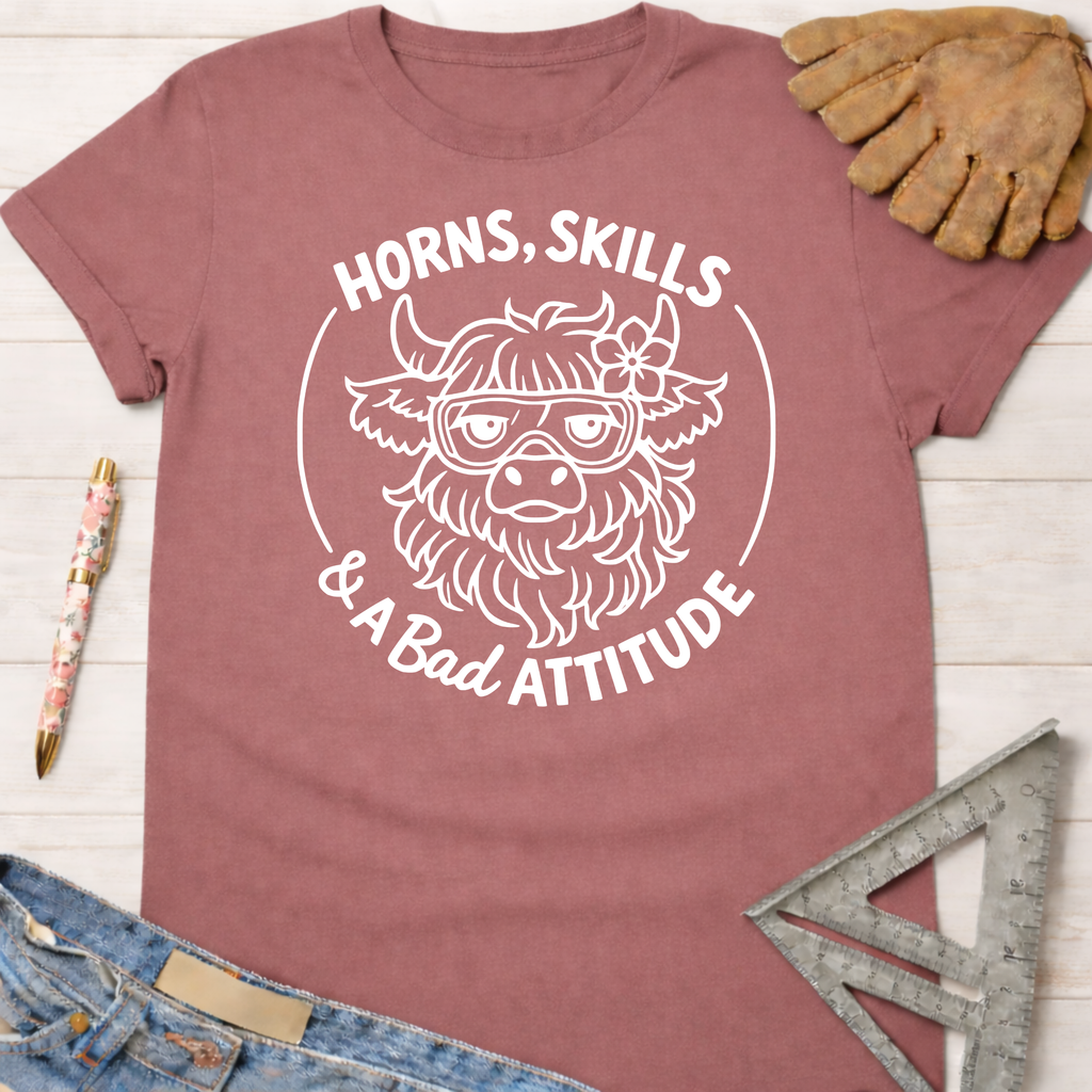 Women's funny woodworking graphic tee shirt for female woodworkers, makers, and DIY builders — Sawdust & Ponytails. Mauve t-shirt with a white graphic of a horned cow wearing goggles and a flower, text "Horns, Skills & A Bad Attitude.