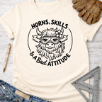 Women's funny woodworking graphic tee shirt for female woodworkers, makers, and DIY builders — Sawdust & Ponytails. Cream t-shirt with "Horns, Skills & A Bad Attitude" highland cow graphic.