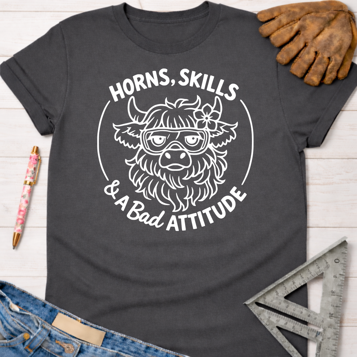 Charcoal gray women's funny woodworking graphic tee with "Horns, Skills & A Bad Attitude" text and a cow wearing safety goggles.