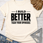 Women's funny woodworking graphic tee shirt for female woodworkers, makers, and DIY builders — Sawdust & Ponytails. Cream t-shirt with "I BUILD BETTER THAN YOUR OPINIONS" in black text.