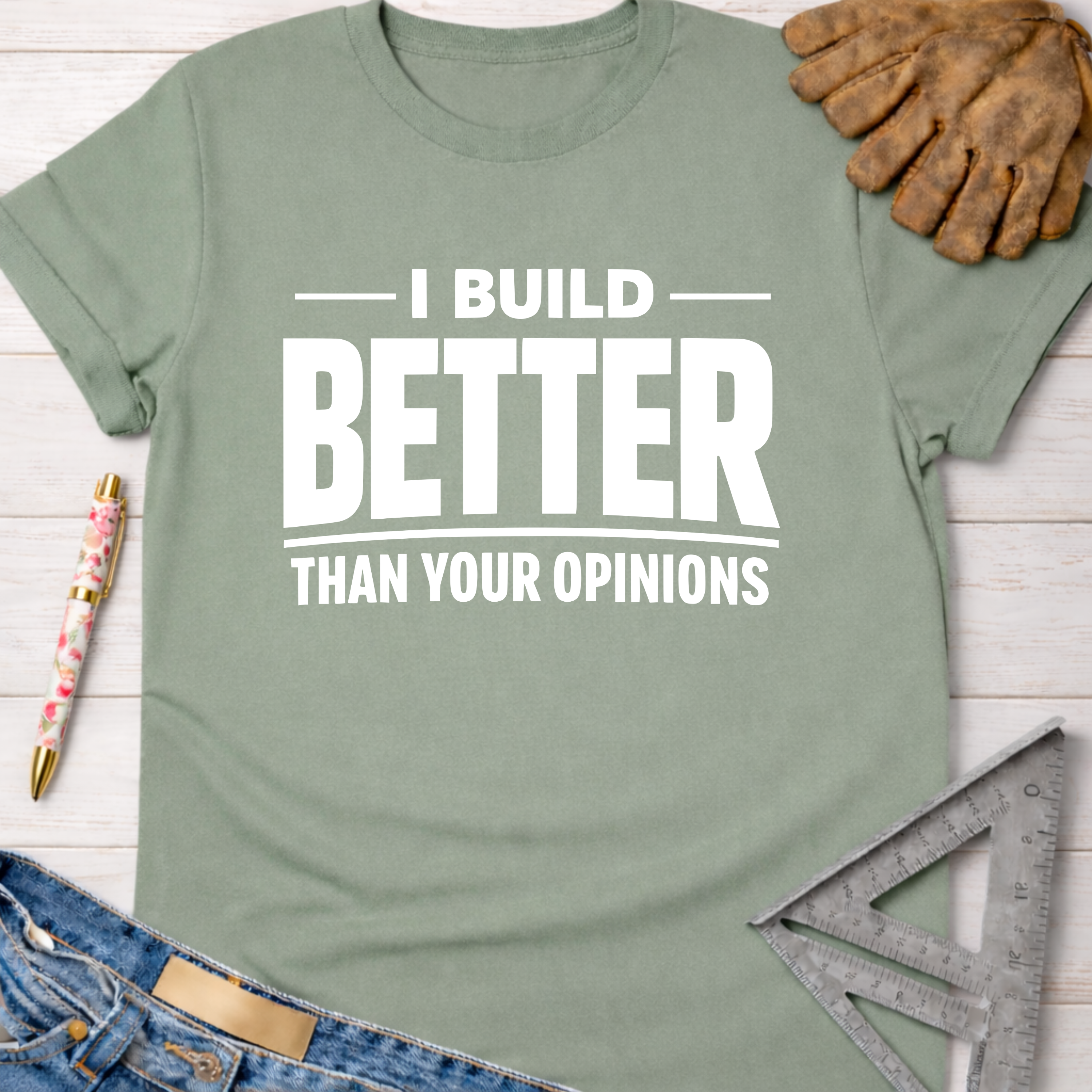 Women's funny woodworking graphic tee shirt for female woodworkers, makers, and DIY builders — Sawdust & Ponytails. Sage green t-shirt with "I BUILD BETTER THAN YOUR OPINIONS" in white text.