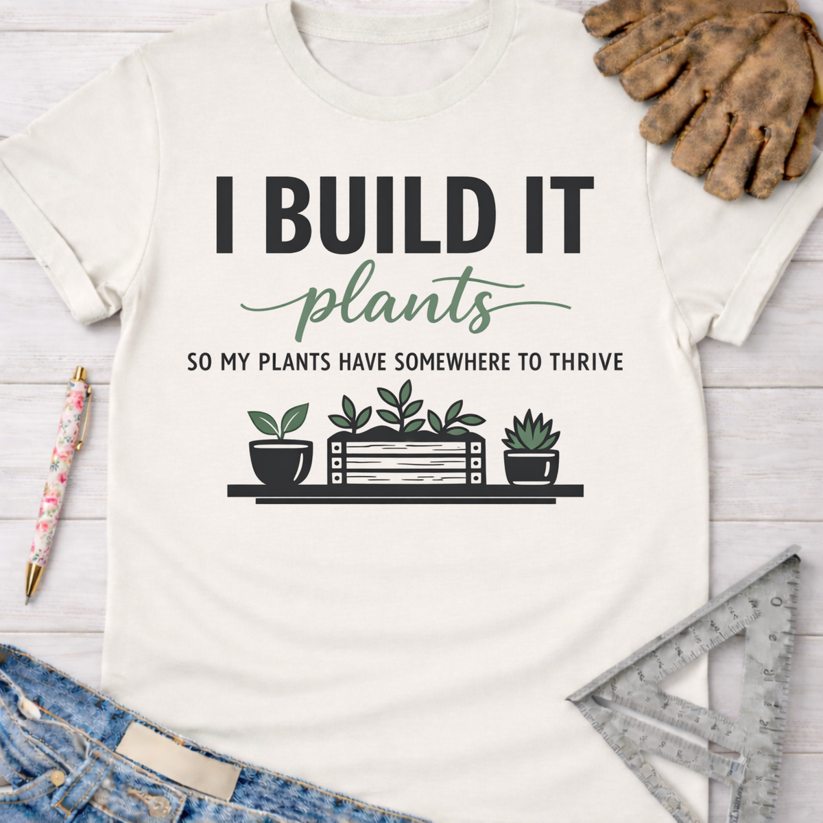 Women's funny woodworking graphic tee shirt for female woodworkers, makers, and DIY builders — Sawdust & Ponytails. White cotton tee with "I BUILD IT plants SO MY PLANTS HAVE SOMEWHERE TO THRIVE" graphic.