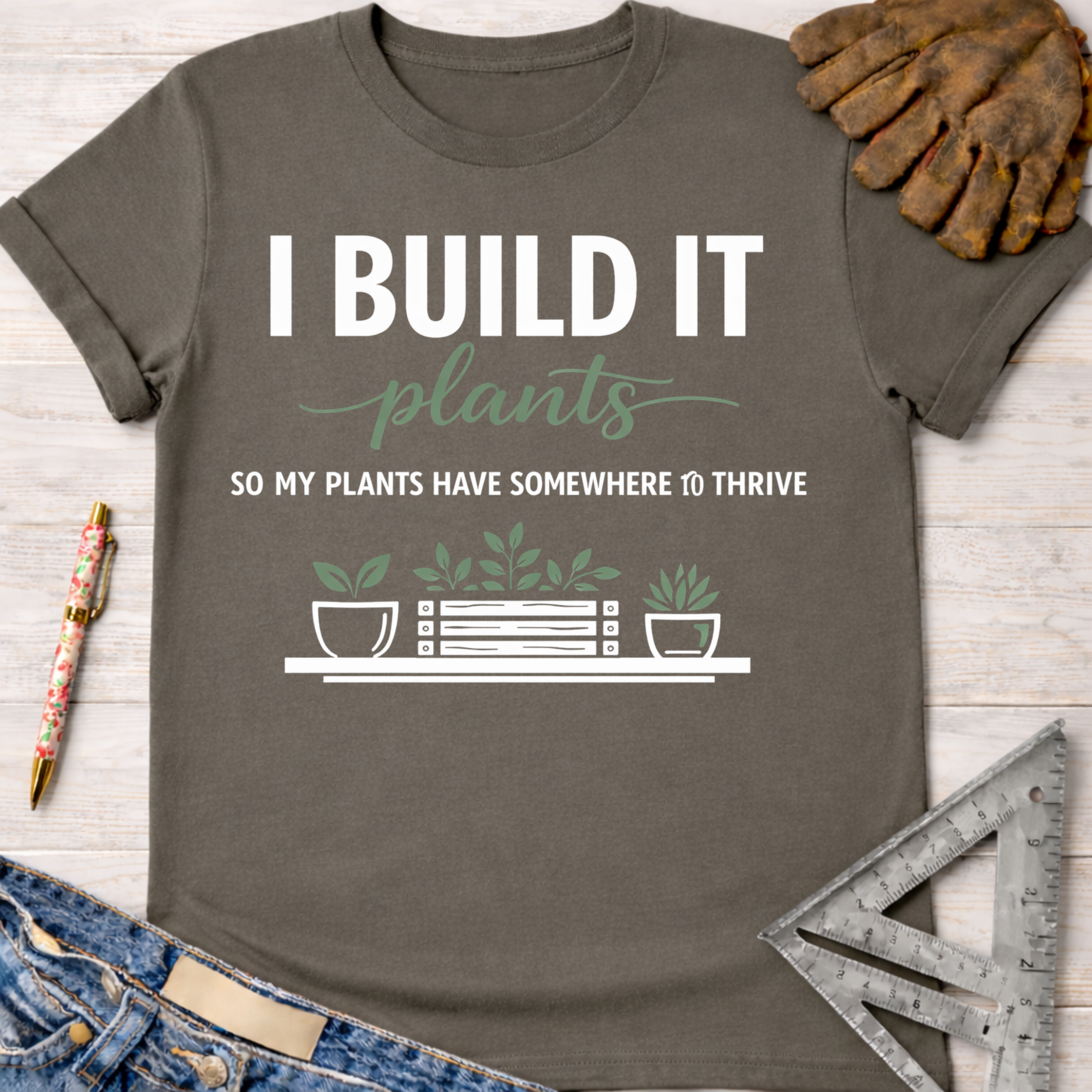 Women's funny woodworking graphic tee shirt for female woodworkers, makers, and DIY builders — Sawdust & Ponytails. Dark gray cotton tee with "I BUILD IT plants SO MY PLANTS HAVE SOMEWHERE TO THRIVE" graphic.