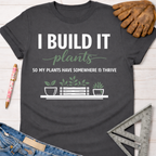 Women's funny woodworking graphic tee shirt for female woodworkers, makers, and DIY builders — Sawdust & Ponytails. Dark gray cotton t-shirt with "I BUILD IT plants SO MY PLANTS HAVE SOMEWHERE TO THRIVE" graphic.
