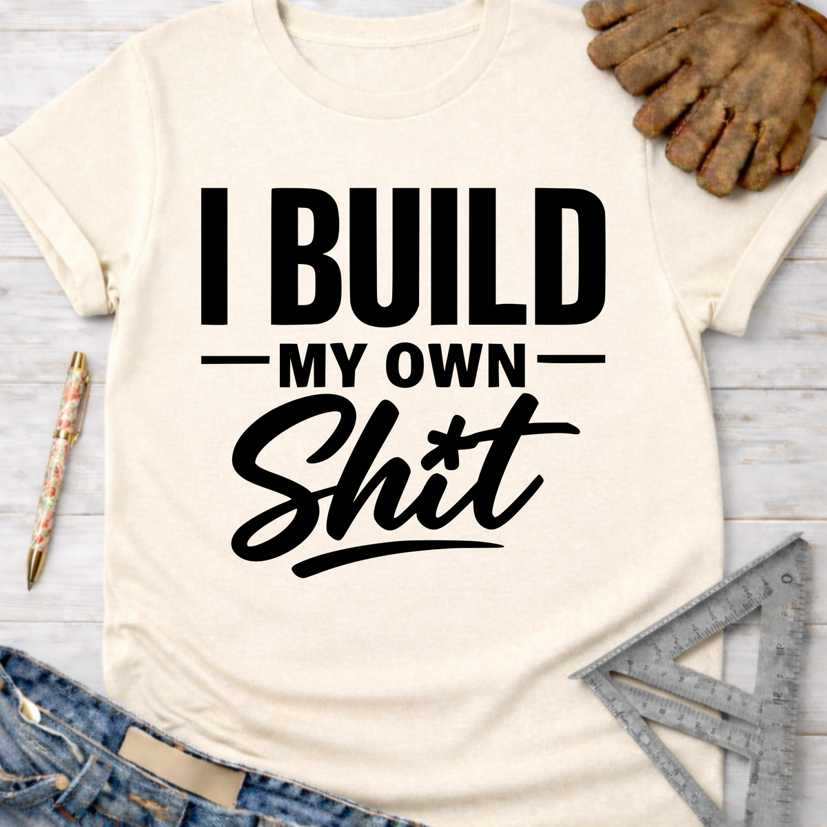 Women's funny woodworking graphic tee shirt for female woodworkers, makers, and DIY builders — Sawdust & Ponytails. Cream t-shirt with "I BUILD MY OWN Shit" in bold black text.