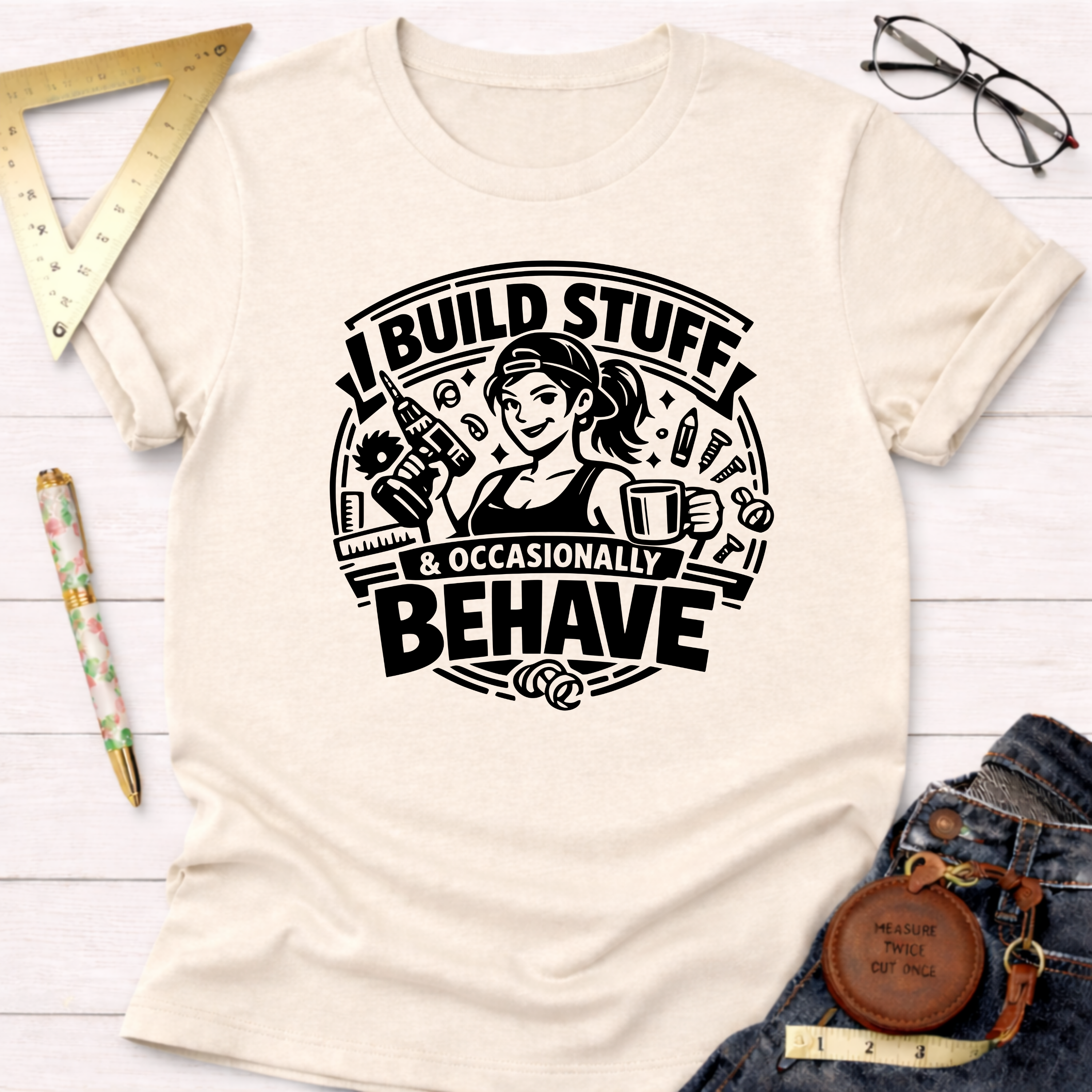 Cream "I Build Stuff & Occasionally Behave" graphic tee with a woman holding a drill and coffee.