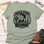 Light olive green cotton t-shirt with "I Build Stuff & Occasionally Behave" graphic featuring a woman with a drill and coffee.