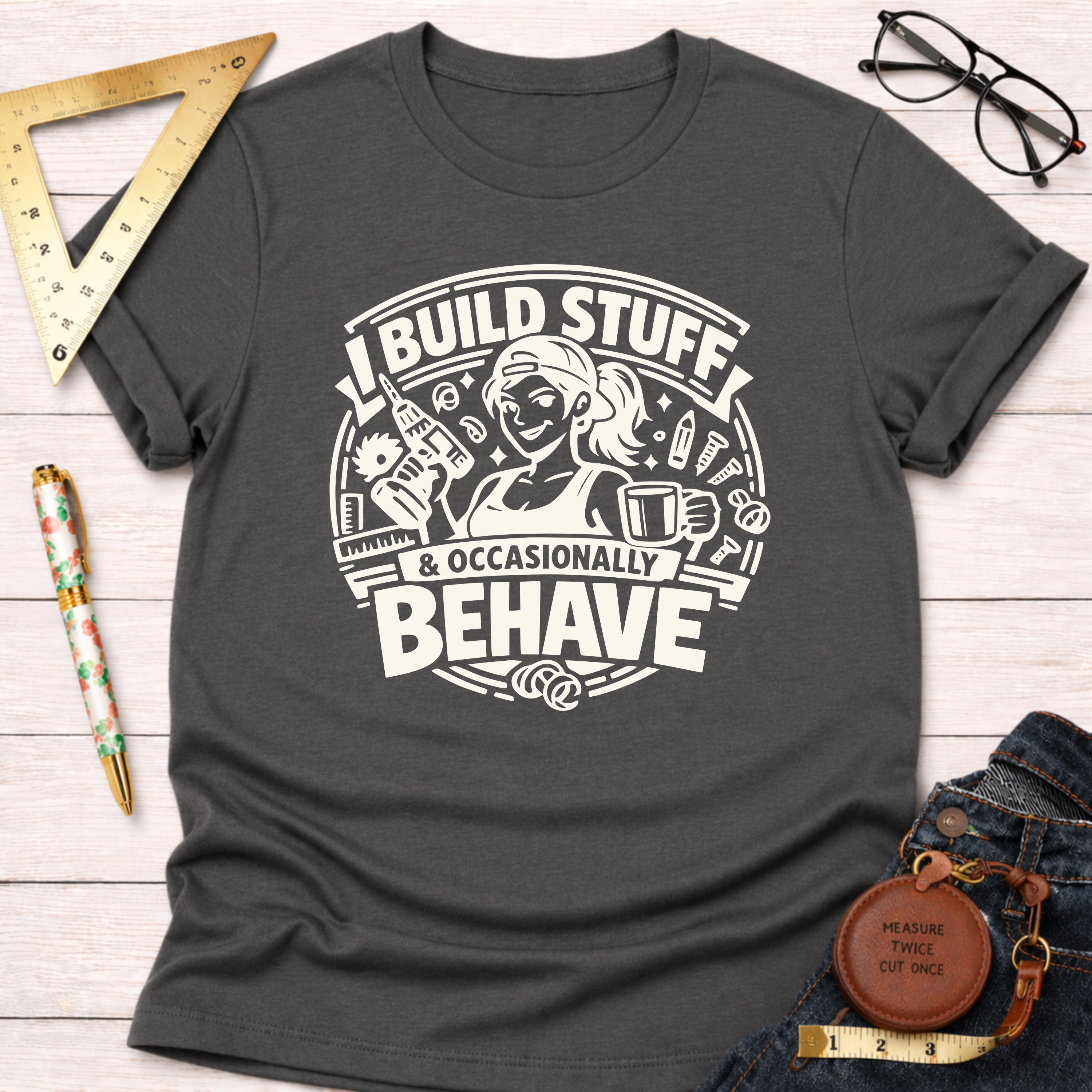Charcoal gray cotton t-shirt with "I Build Stuff & Occasionally Behave" graphic featuring a woman with tools.