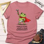 Women's funny woodworking graphic tee shirt for female woodworkers, makers, and DIY builders — Sawdust & Ponytails. Pink cotton tee with a frog in a cape holding a hammer and saw, text "I BUILD STUFF. WHAT'S YOUR SUPERPOWER?".